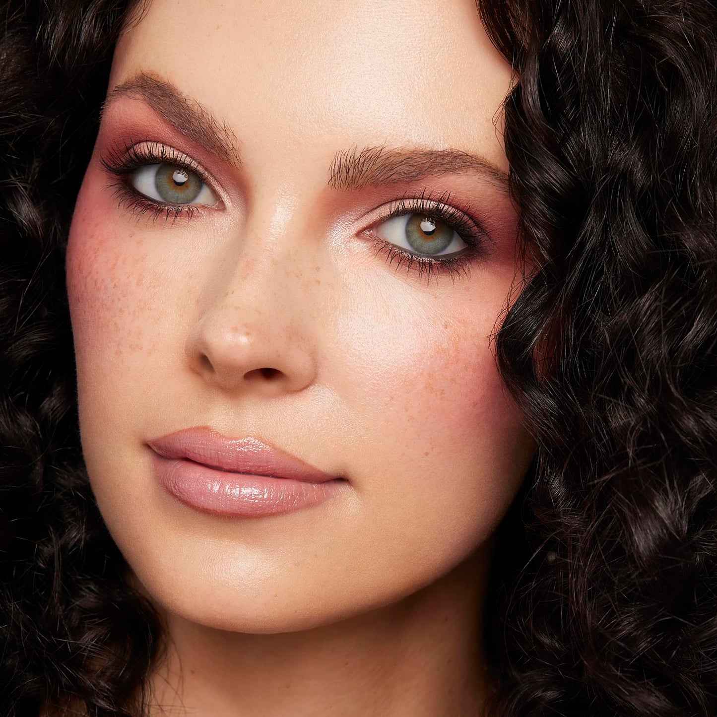 Rosy mauve eyeshadow with soft brown crease and inner-corner shimmer on a model, showcasing the Coconut BB ColourPop Shadow Palette Set, with long lashes, nude glossy lips, freckles, and dark curls in a studio close-up.