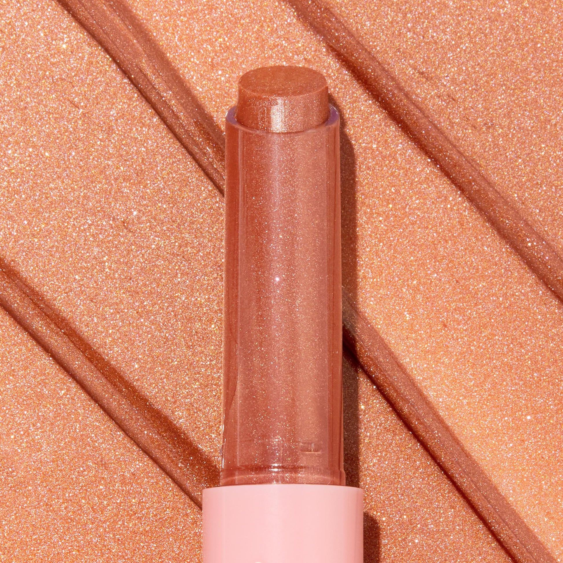 Angel Baby ColourPop So Juicy Plumping Gloss Balm with Peptides extends from a pink tube, the shimmery peach-nude bullet catching light, shown atop matching metallic swatches to highlight its glossy, plumping finish.